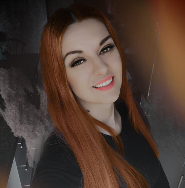 Andželija Zykaitė Raudonplaukė moteris sėdi prie stalo, apsupta simbolinės dvasinės aplinkos – žvakės, džiovinti augalai, piešiniai. Jos žvilgsnis – ramus ir gilus, kviečiantis į tylų ryšį su savimi.